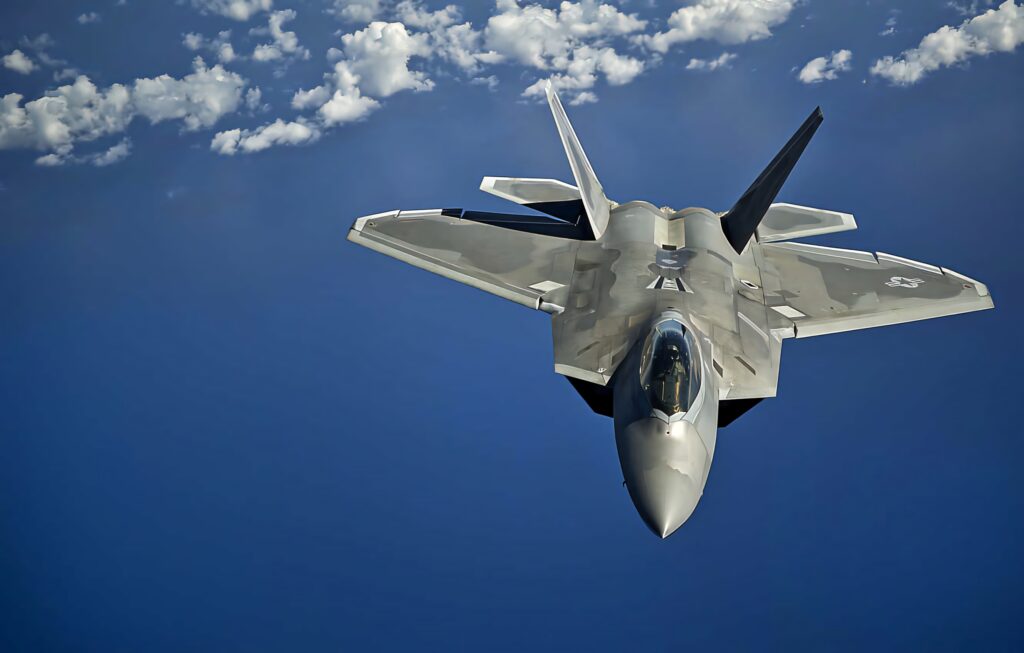 Lockheed Martin F-22 Raptor soaring above clouds with sharp stealth design in blue sky Wallpaper