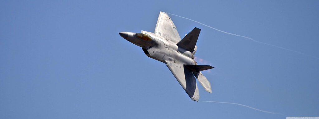 Lockheed Martin F-22 Raptor stealth fighter jet soaring in clear blue sky with contrails wallpaper