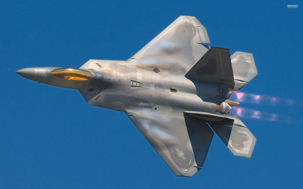 Lockheed Martin F-22 Raptor soaring with afterburners in clear blue sky showcasing stealth design Wallpaper