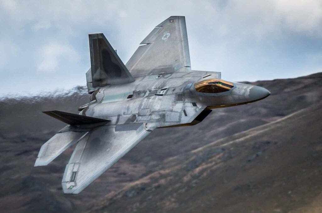 Lockheed Martin F-22 Raptor flying low over mountains with stealth design and gray camouflage Wallpaper