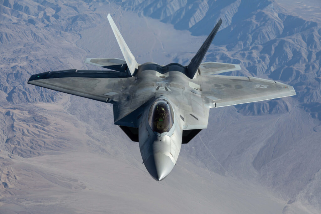 Lockheed Martin F-22 Raptor stealth fighter flying over rugged mountains with blue gray tones Wallpaper