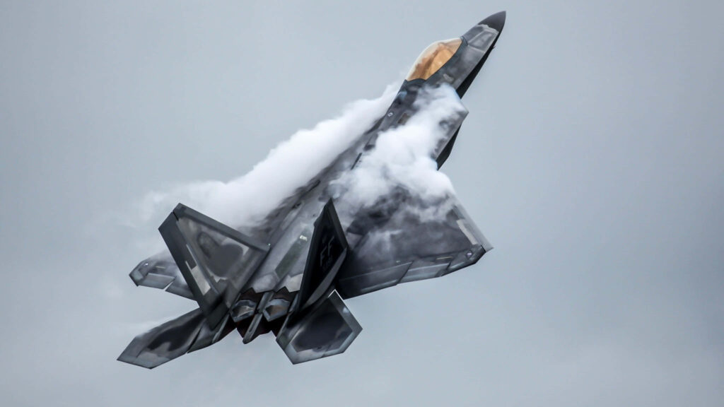 Lockheed Martin F-22 Raptor soaring with vapor trails against gray sky showcasing stealth design Wallpaper