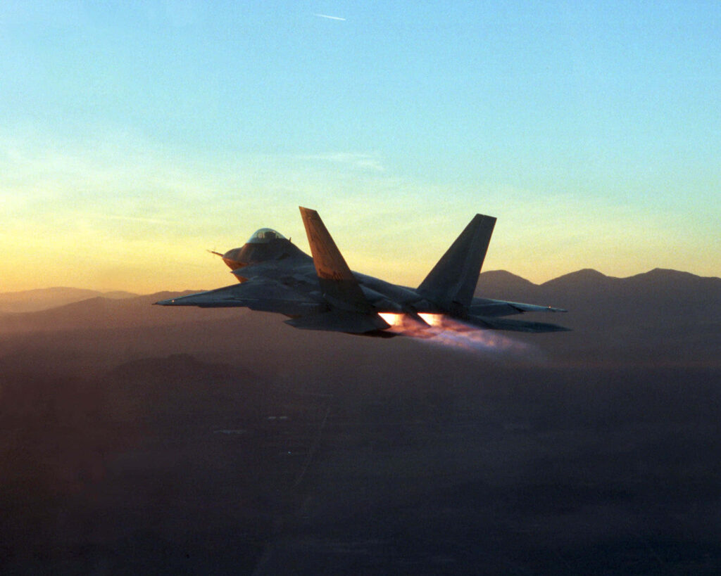 Lockheed Martin F-22 Raptor jet with blazing afterburners flying over mountains at sunset Wallpaper