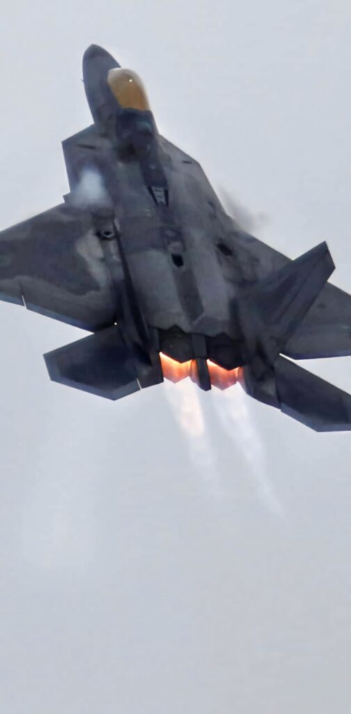 Lockheed Martin F-22 Raptor jet with glowing afterburners soaring in gray sky dynamic wallpaper