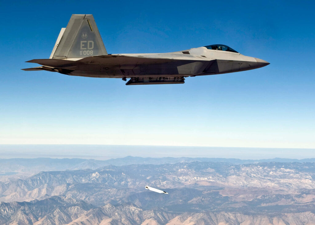 Lockheed Martin F-22 Raptor jet releasing missile over mountains in clear blue sky wallpaper