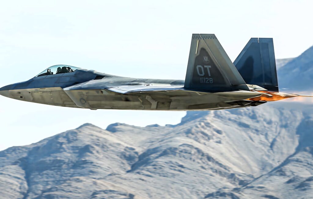 Lockheed Martin F-22 Raptor in flight with twin afterburners over rugged mountains wallpaper