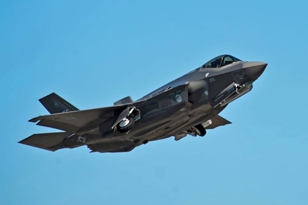Lockheed Martin F-35 fighter jet in flight against blue sky showcasing stealth design and technology Wallpaper