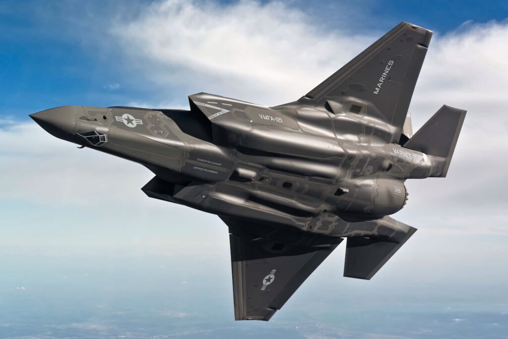 Lockheed Martin F-35 stealth fighter jet soaring in blue sky with dark gray camouflage and insignia Wallpaper