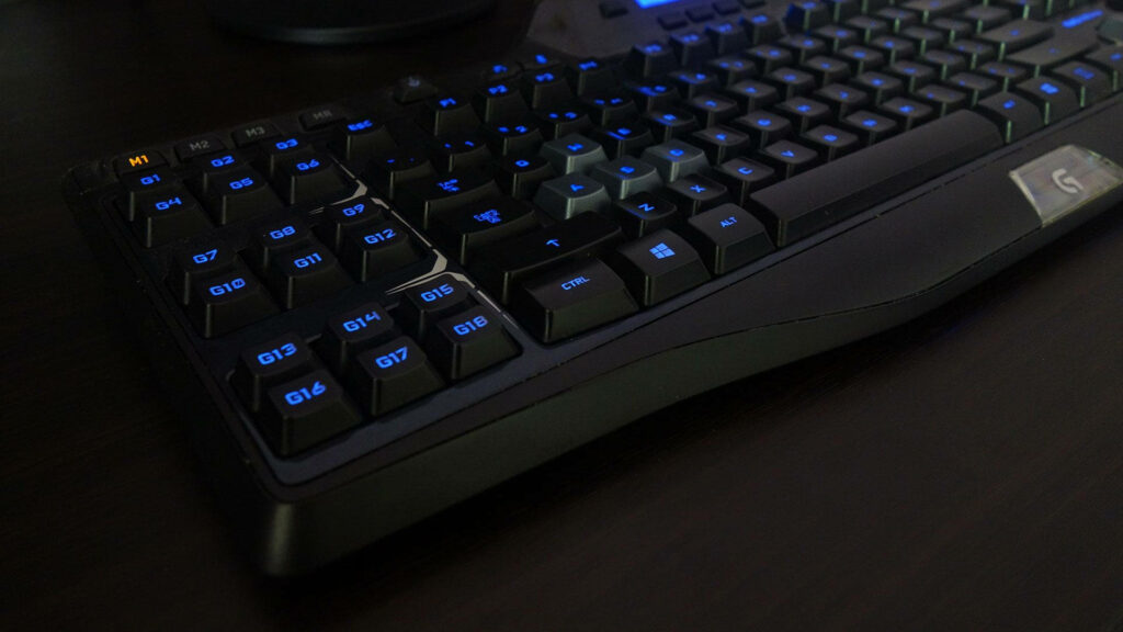 Close-up of Logitech black gaming keyboard with blue backlit keys on dark modern background Wallpaper