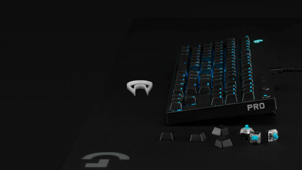 Logitech mechanical keyboard with blue backlight on dark surface with keycap puller and switches Wallpaper