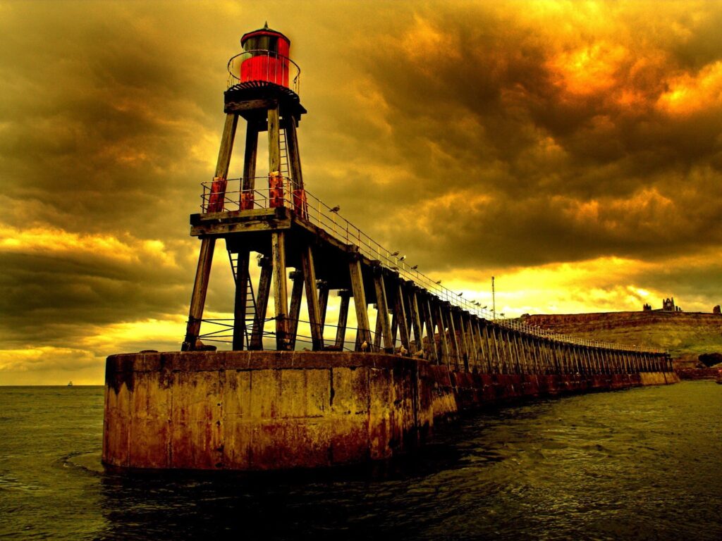Lone beacon on long pier under dramatic cloudy sky moody golden tones wallpaper background