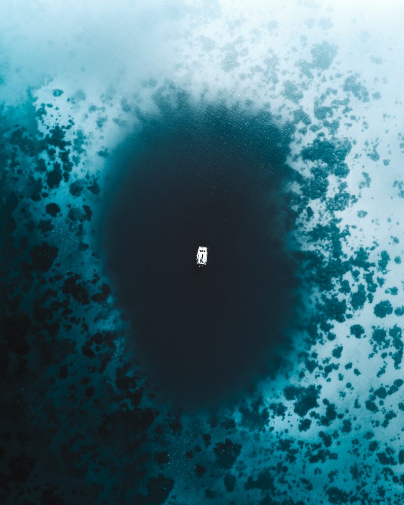 Aerial view of lone boat on deep blue ocean with turquoise reefs and vast sea background wallpaper