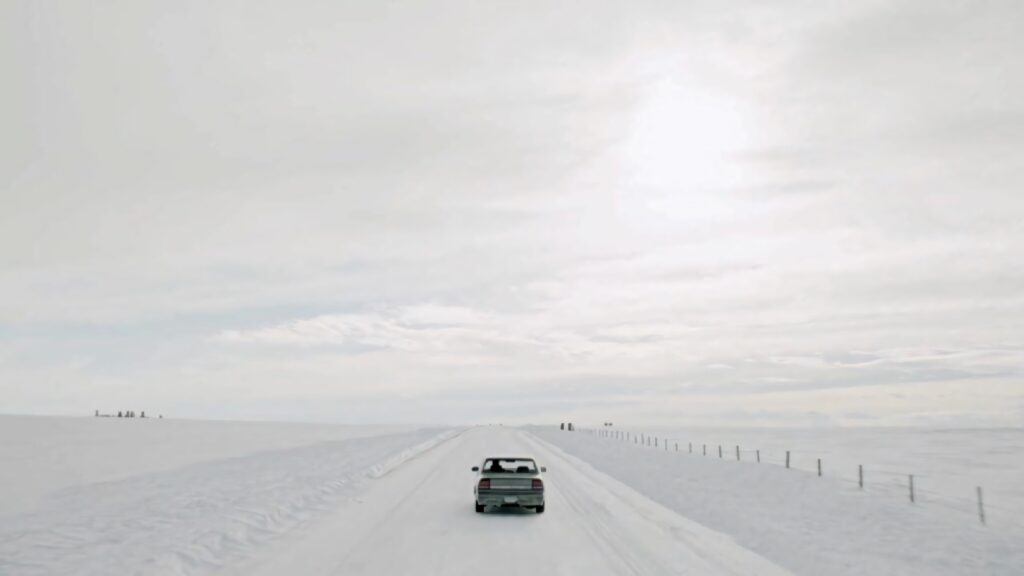 Lone car on snowy desolate road under overcast sky evoking Fargo crime series atmosphere wallpaper