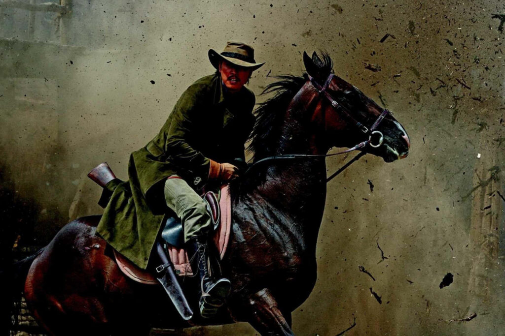 Lone cowboy riding horse through dusty Wild West landscape rugged coat wide-brimmed hat wallpaper