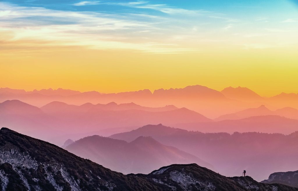 Lone hiker on mountain ridge at sunset with rainbow mist and pastel purple pink sky background Wallpaper