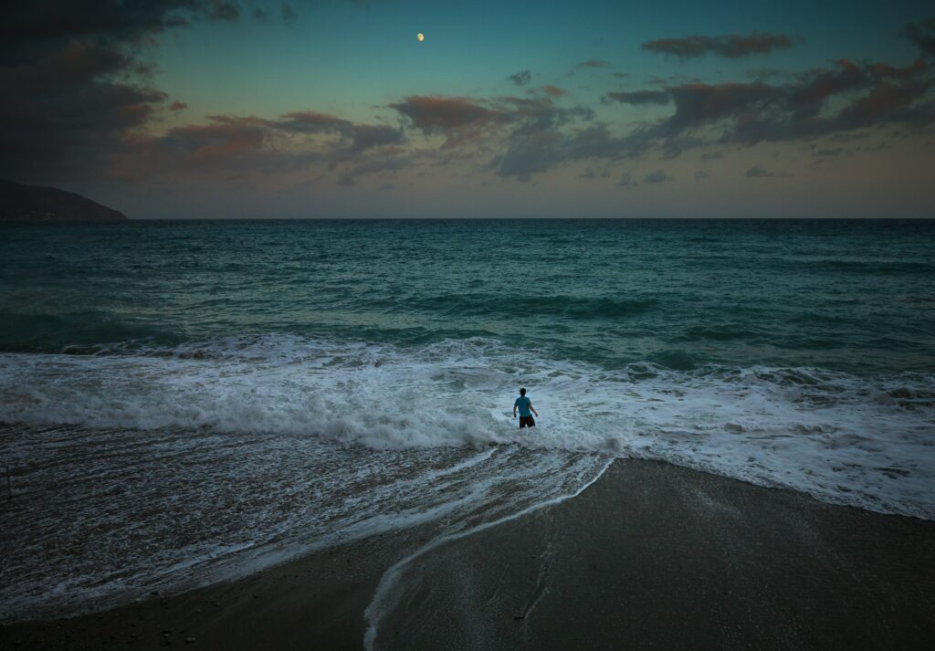 Man standing on shore facing powerful sea waves under dramatic twilight sky wallpaper background