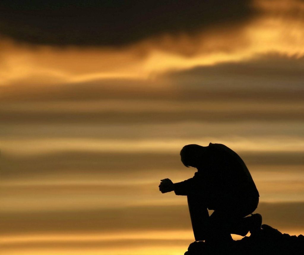 Silhouette of man kneeling in prayer at golden sunset sky peaceful reflective wallpaper background