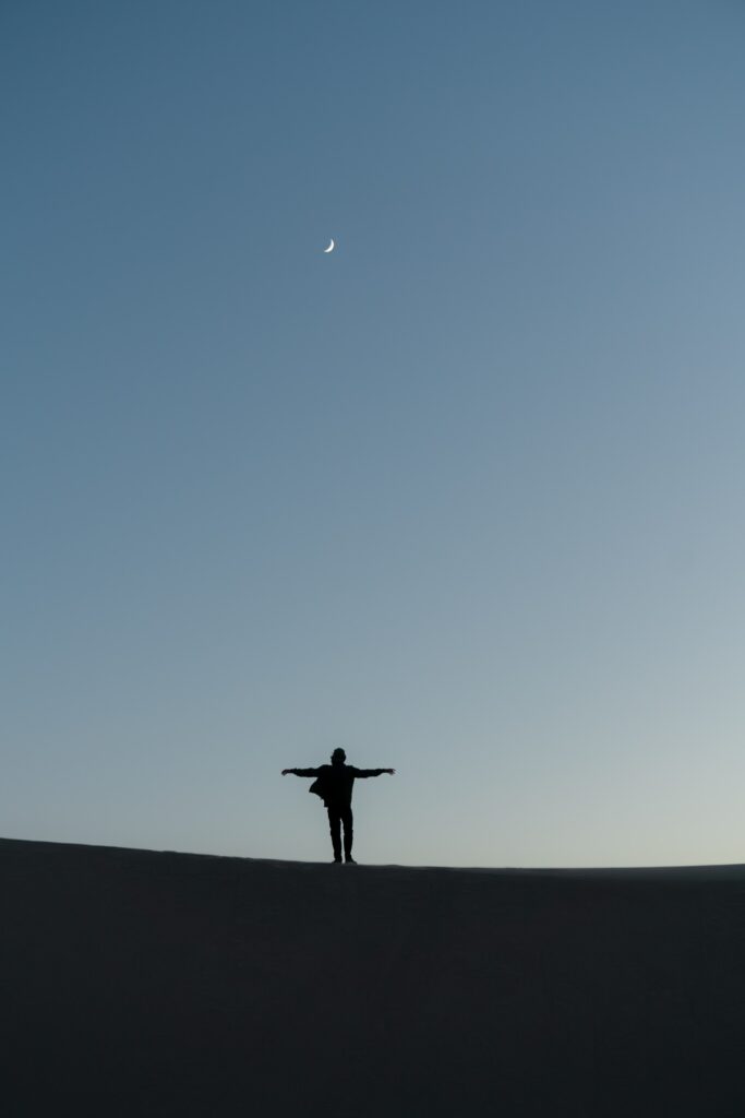 Silhouette of a man with outstretched arms under crescent moon sky symbolizing freedom and solitude Wallpaper