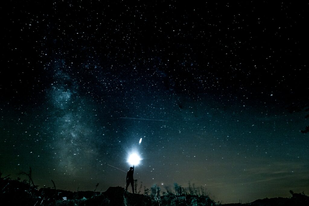 Silhouette of man under vast starry sky with glowing cosmic light and sparkling stars background Wallpaper