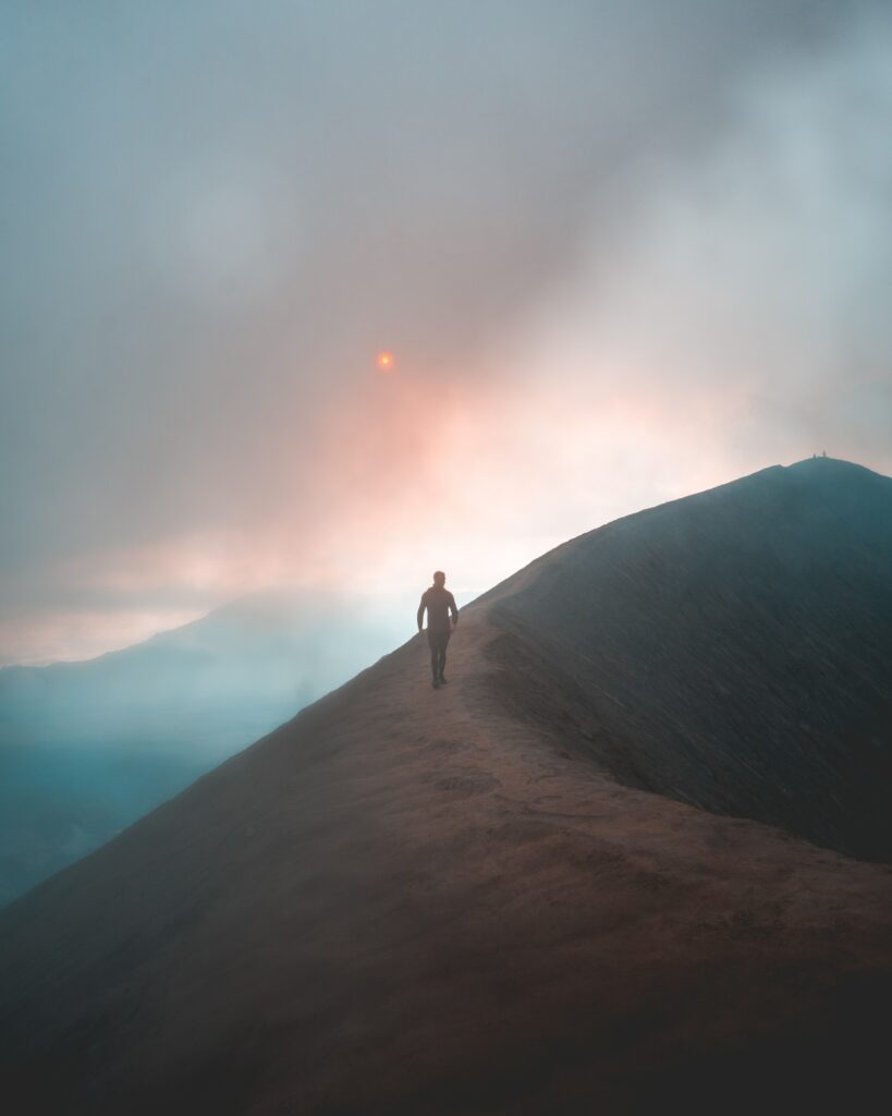 Lone man walking foggy mountain ridge at sunrise tranquil sky blue orange hues wallpaper background