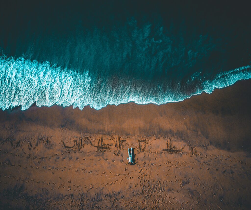 Lone man lying on sandy shore with turquoise waves rolling gently captured from above Wallpaper