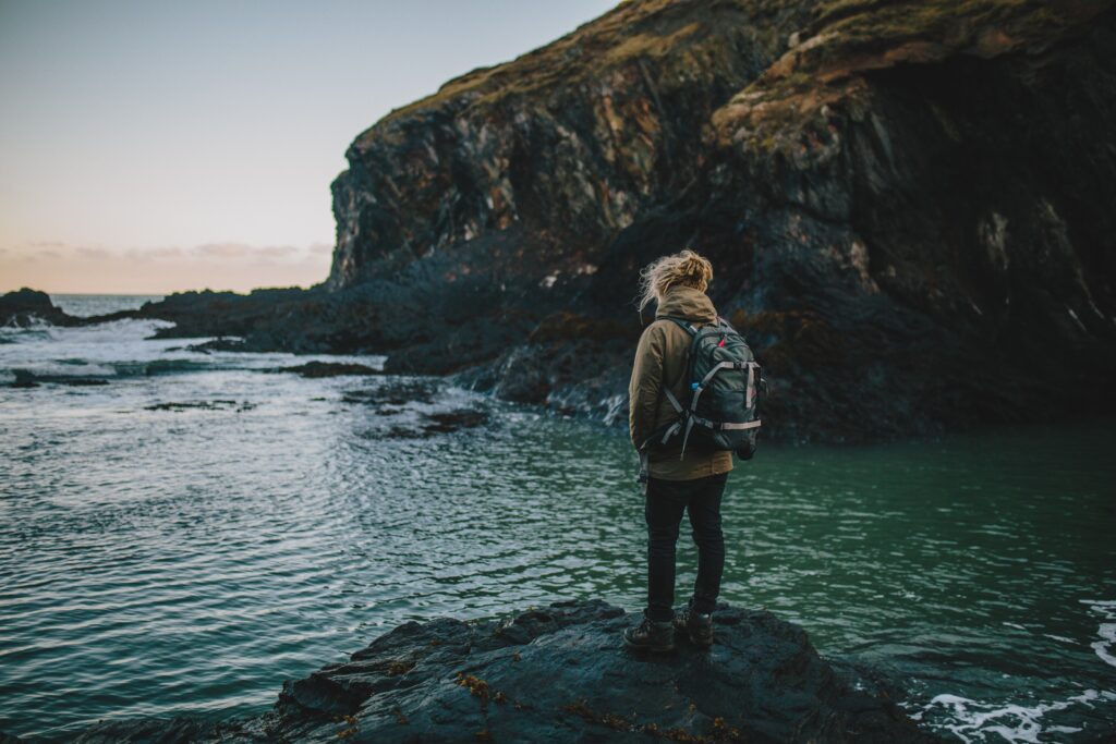 Tourist on rugged coastal rocks gazing at dramatic cliffs under clear sky scenic wallpaper background