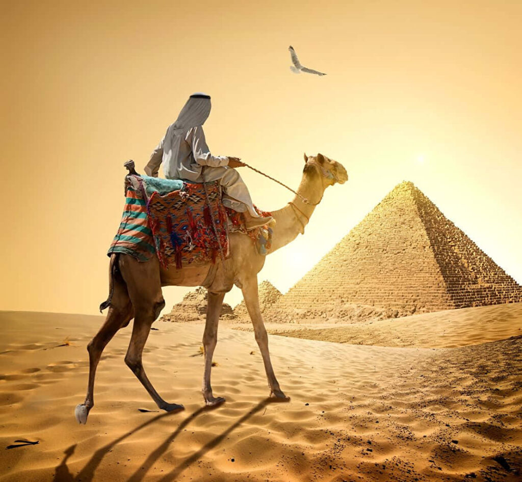 Lone traveler on camel crossing golden desert sands toward ancient pyramids under glowing sun Wallpaper