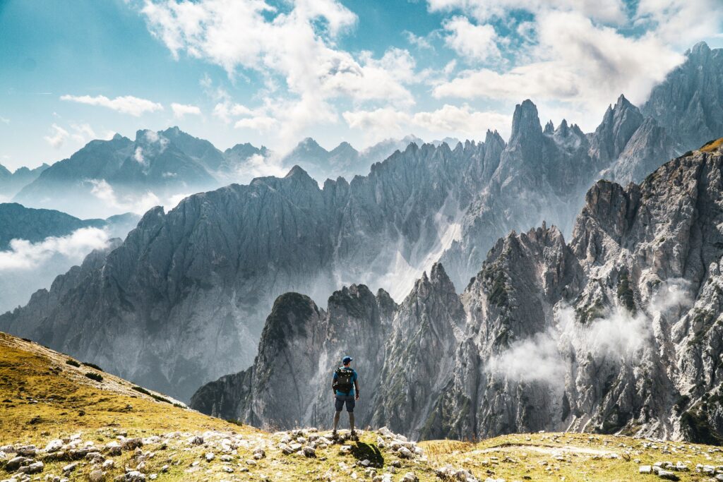 Lone traveler on sunlit Italian mountain ridge surrounded by rocky peaks and drifting clouds Wallpaper