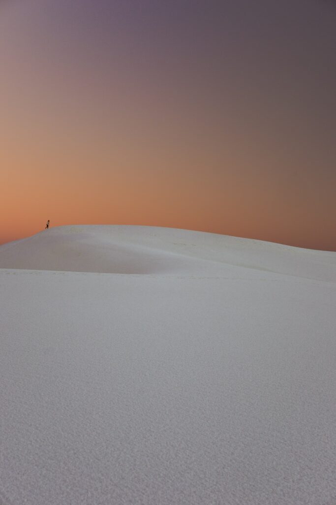 Lone wanderer crosses glowing white sand dunes at sunset in White Sands National Monument US Wallpaper