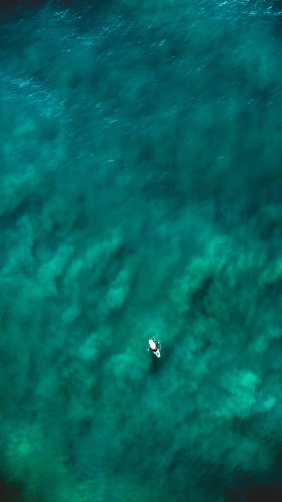 Aerial view of a lone boat on deep turquoise sea with gentle waves and clear water patterns Wallpaper