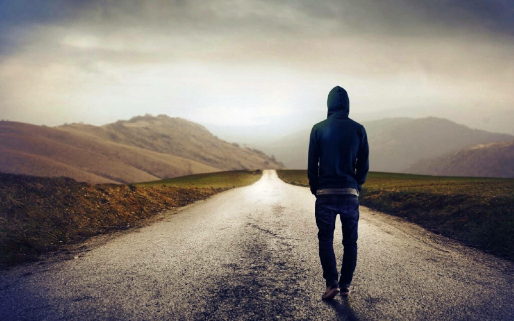 Solitary Stroll: Mysterious Figure Adorned in Hoodie Jacket Treads Solitarily on Dreary Path - Captivating Backdrop Image Wallpaper