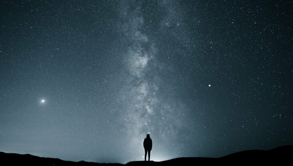 Lonely Explorer: A Man Silhouette Gazing at the Majestic Milky Way and Starry Sky - QHD Wallpaper Background Photo in QHD 2K 2540x1444 Resolution