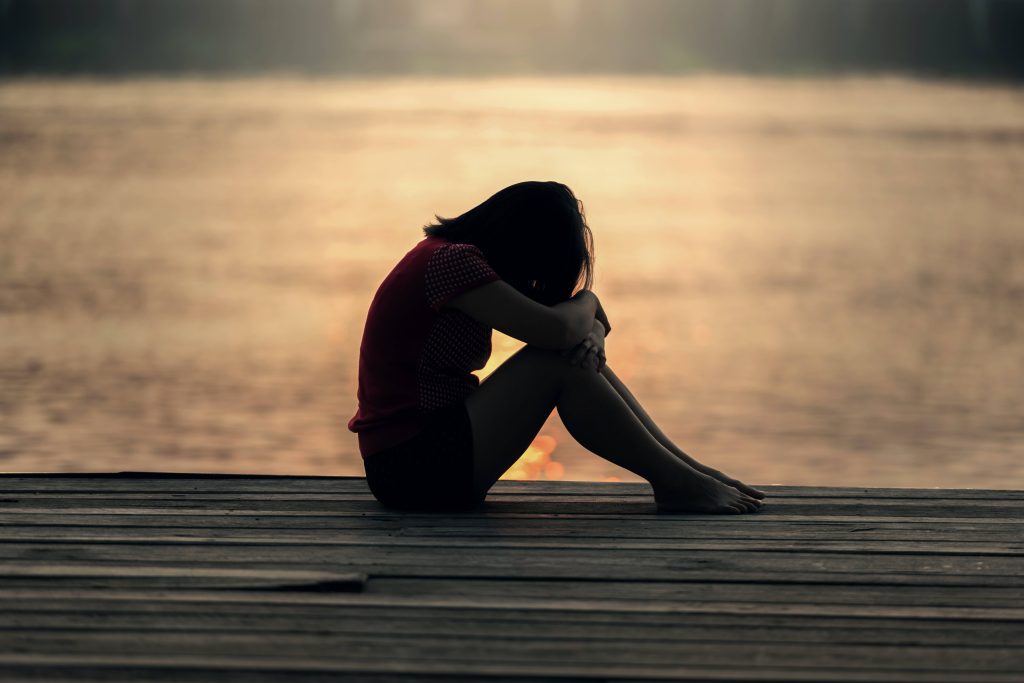 Silhouette of a young woman sitting curled on dock at sunset evoking sad lonely mood wallpaper