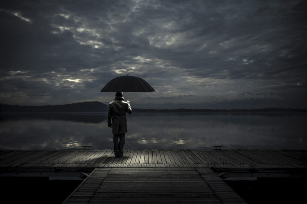Solitude and Sorrow: A Lone Man Finds Love and Protection Under His Umbrella Amidst the Sad Waters and Skies - An Emotional Wallpaper Background Photo