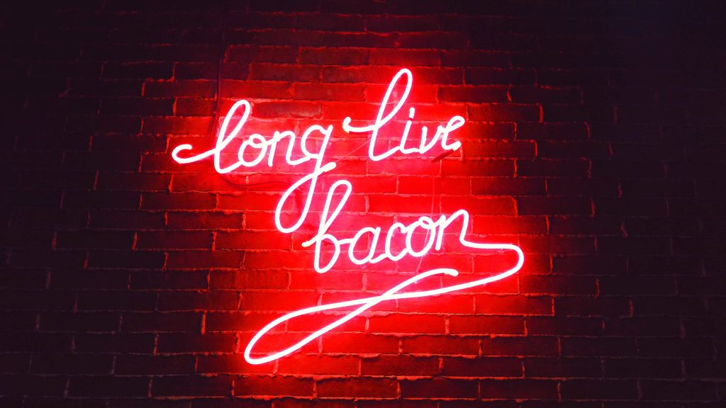 Vibrant red neon long live bacon sign glowing on dark rustic brick wall wallpaper background