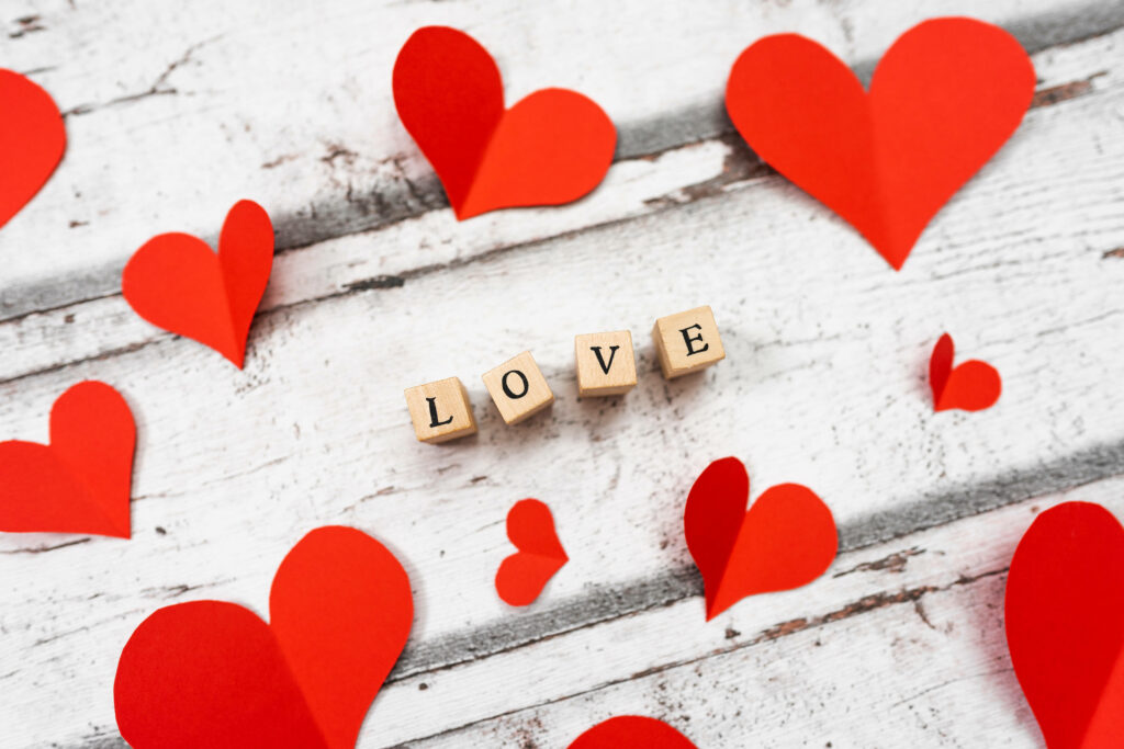 Romantic Letter Game: Love Spelled in Scrabble Tiles atop Rustic White Wood with Red Heart Decorations Wallpaper