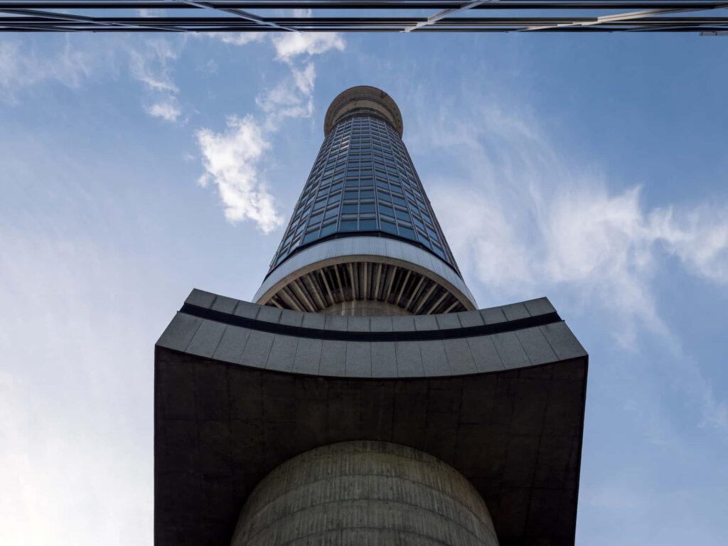 Low-angle view of BT Tower showcasing modern glass and concrete architecture against blue sky Wallpaper