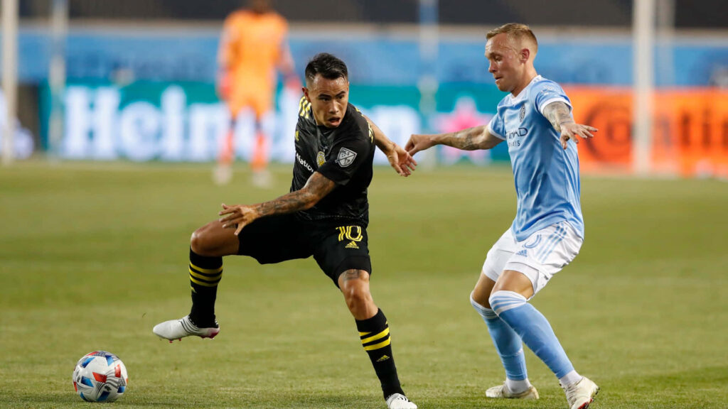 Lucas Zelarayan of Columbus Crew challenges James Sands in intense soccer match under stadium lights Wallpaper