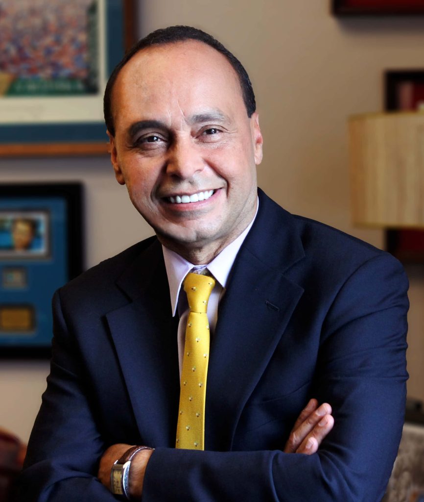 Portrait of former US Representative Luis Gutiérrez smiling in navy suit lavender shirt yellow tie office background Wallpaper