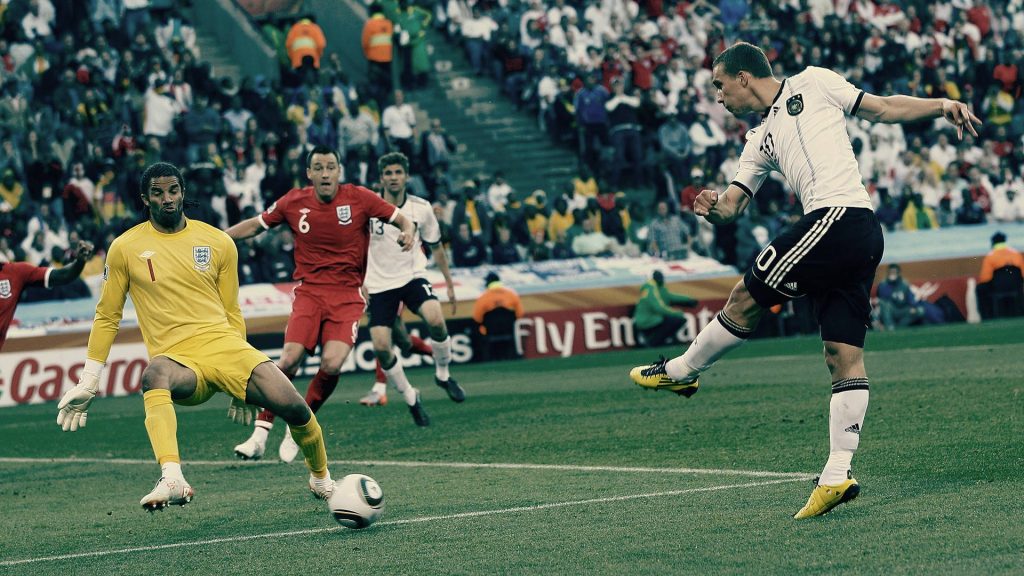 Lukas Podolski shooting goal against England goalkeeper in intense soccer stadium action wallpaper