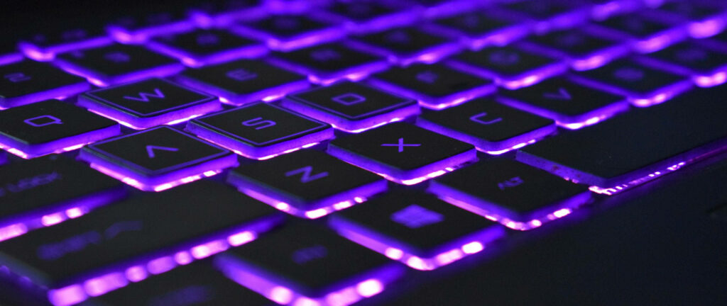 Glowing Violet Neon Illumination on Laptop Keyboard: Captivating Computer Workspace Wallpaper