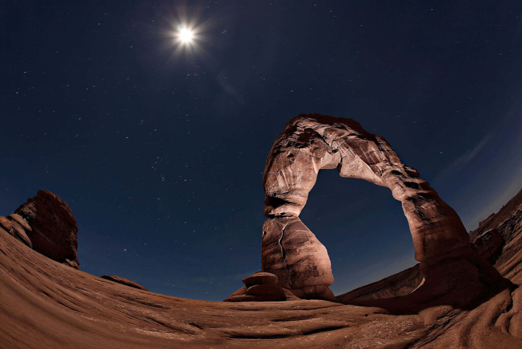 Full moon glowing over Delicate Arch red sandstone under starry night sky nature wallpaper background