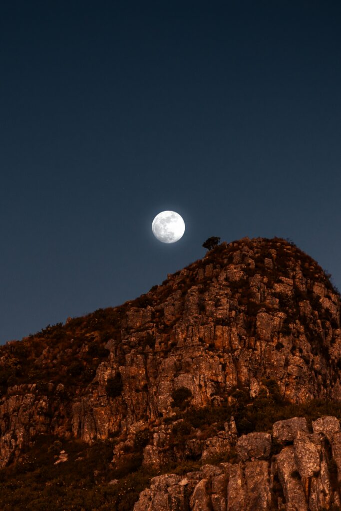 Full moon over rugged rocky mountains under deep night sky creating serene nighttime scene Wallpaper