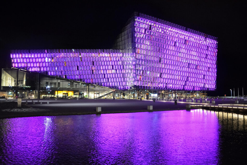 Luminous Waterside Structure: Brilliant Light Purple Windows Illuminate the Night Wallpaper