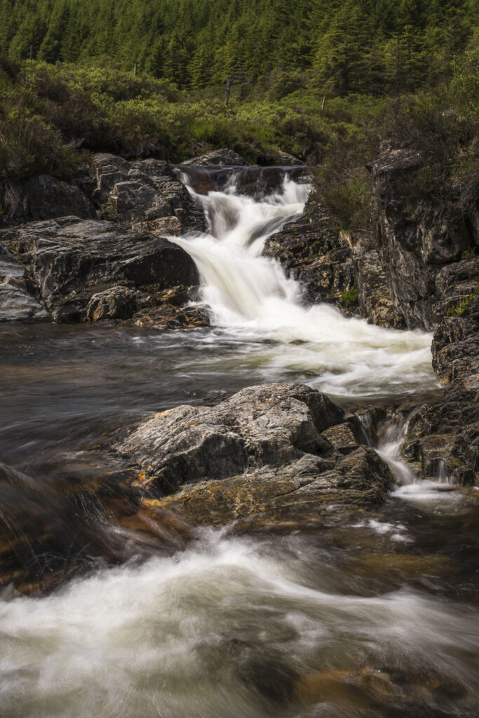 Lively river cascading over smooth stones in lush green forest with rugged rocks wallpaper background