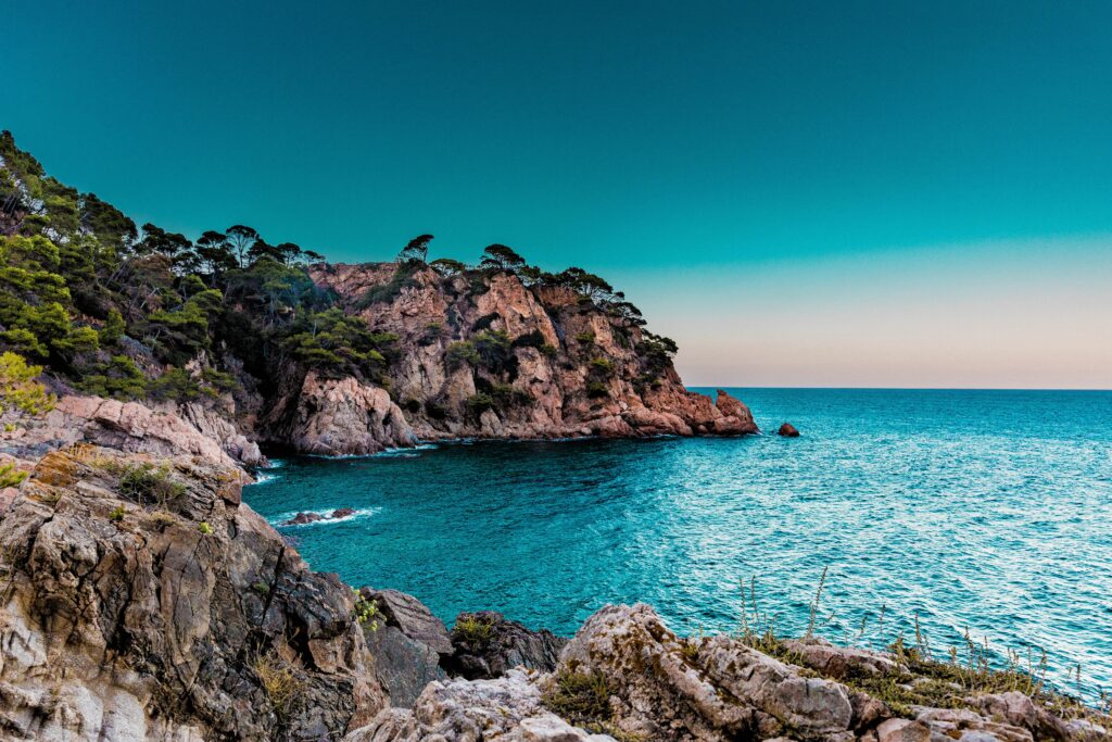Rugged green cliffs by calm blue sea under clear sky natural landscape wallpaper background