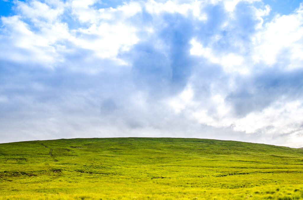 Lush green field and rolling hill under dramatic blue sky with scattered clouds wallpaper background