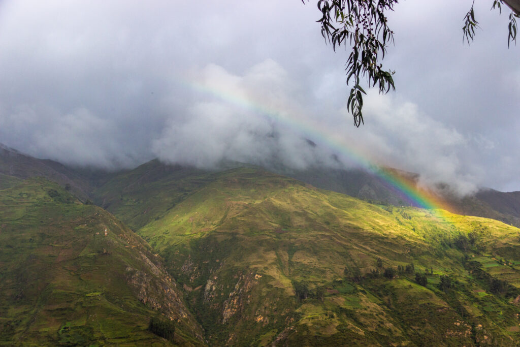 Lush green hills under cloudy sky with vibrant rainbow arching over peaceful natural landscape wallpaper