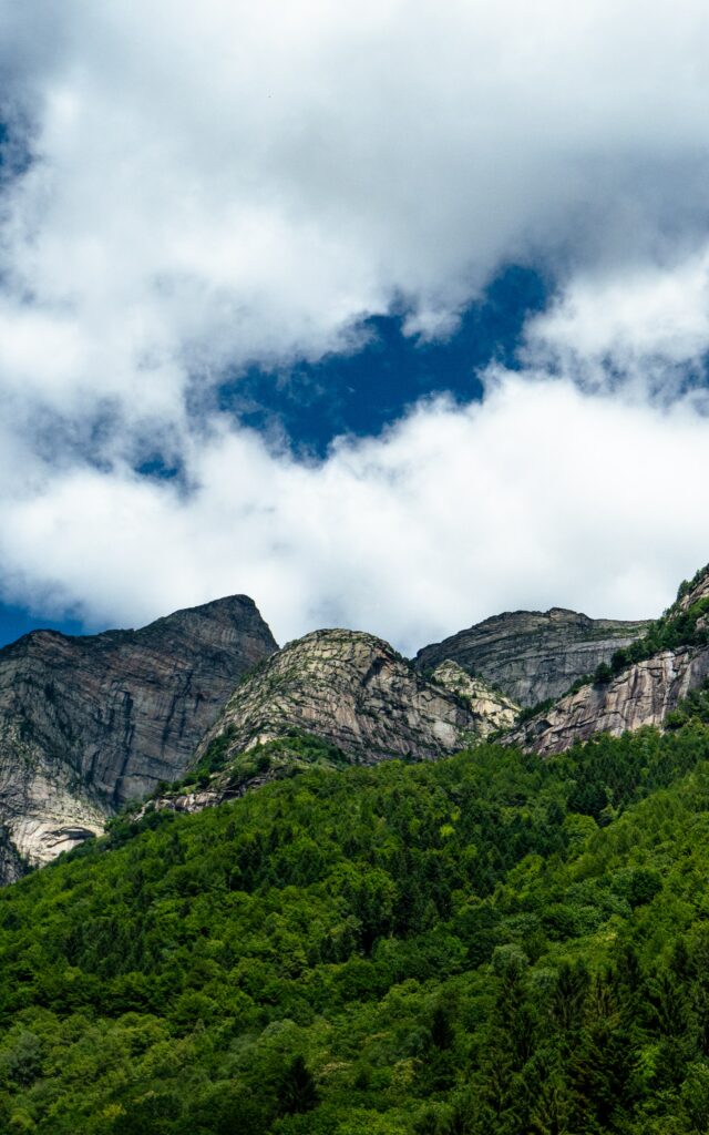 Lush green trees on rugged mountain range under dynamic white clouds nature wallpaper background