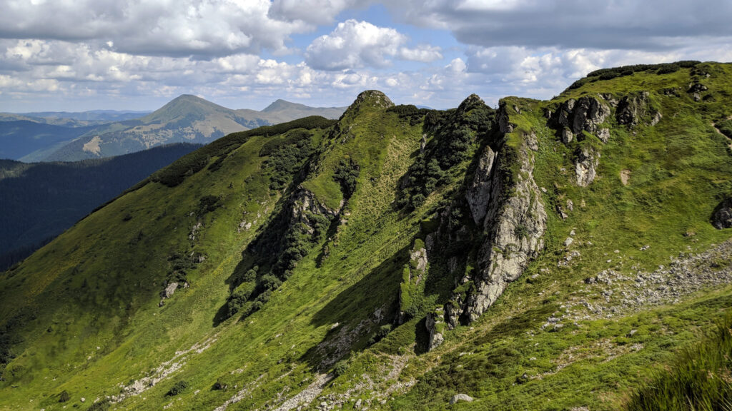 Rolling mountains with lush green slopes and rocky outcrops under a partly cloudy sky wallpaper